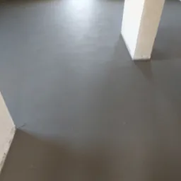 Świeżo wylana, gładka posadzka jastrychowa w pomieszczeniu z surowymi ścianami i kolumną, widoczne drobne włókna w strukturze jastrychu.