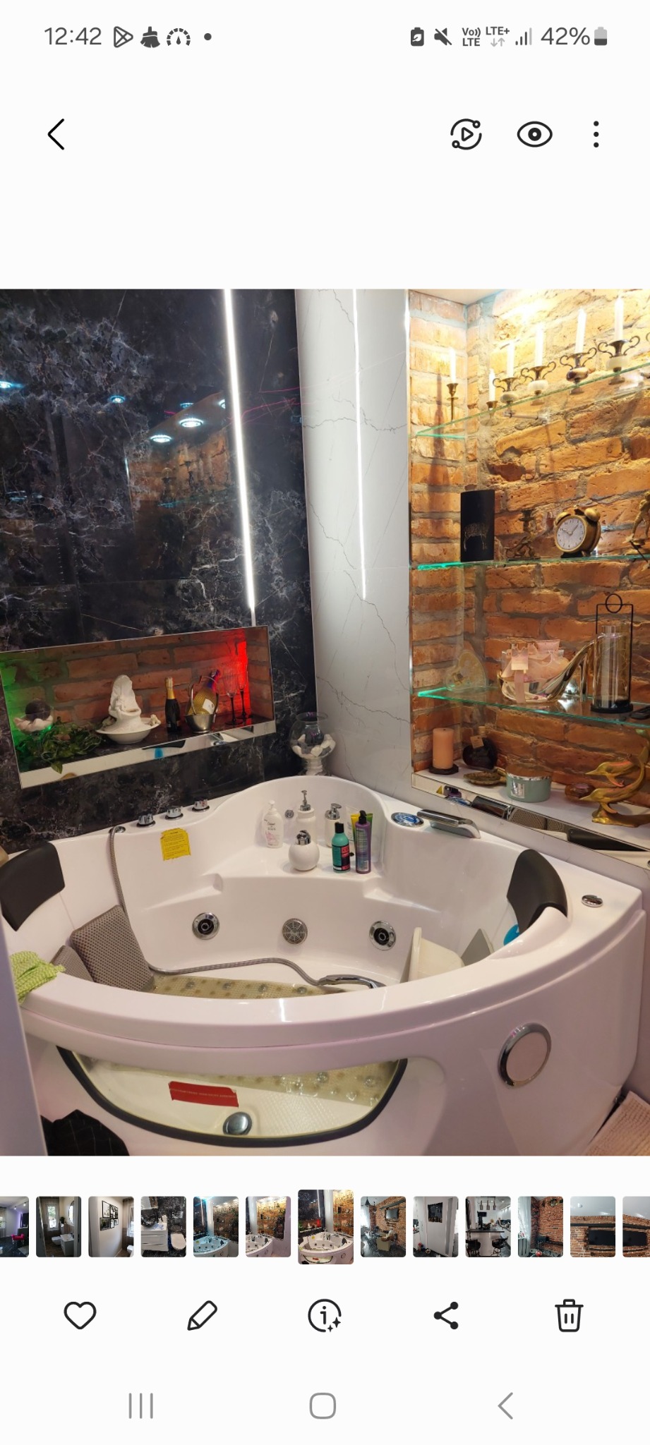 Nowoczesna, narożna wanna z hydromasażem, wypełniona wodą, z widocznymi dyszami, na tle ściany wyłożonej czarnym marmurem i cegłą, z dekoracyjnymi półkami i oświetleniem.