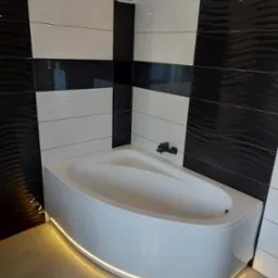 Nowoczesna łazienka z wanną narożną podświetloną taśmą LED, ściany wyłożone czarno-białymi płytkami z falistym wzorem.