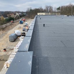 MK Marek Kuznowicz - Widok z góry na nowo pokryty, płaski dach z papy termozgrzewalnej, z widocznymi kominkami wentylacyjnymi i obróbkami blacharskimi na krawędzi, w tle zaparkowane samochody i budynki mieszkalne.