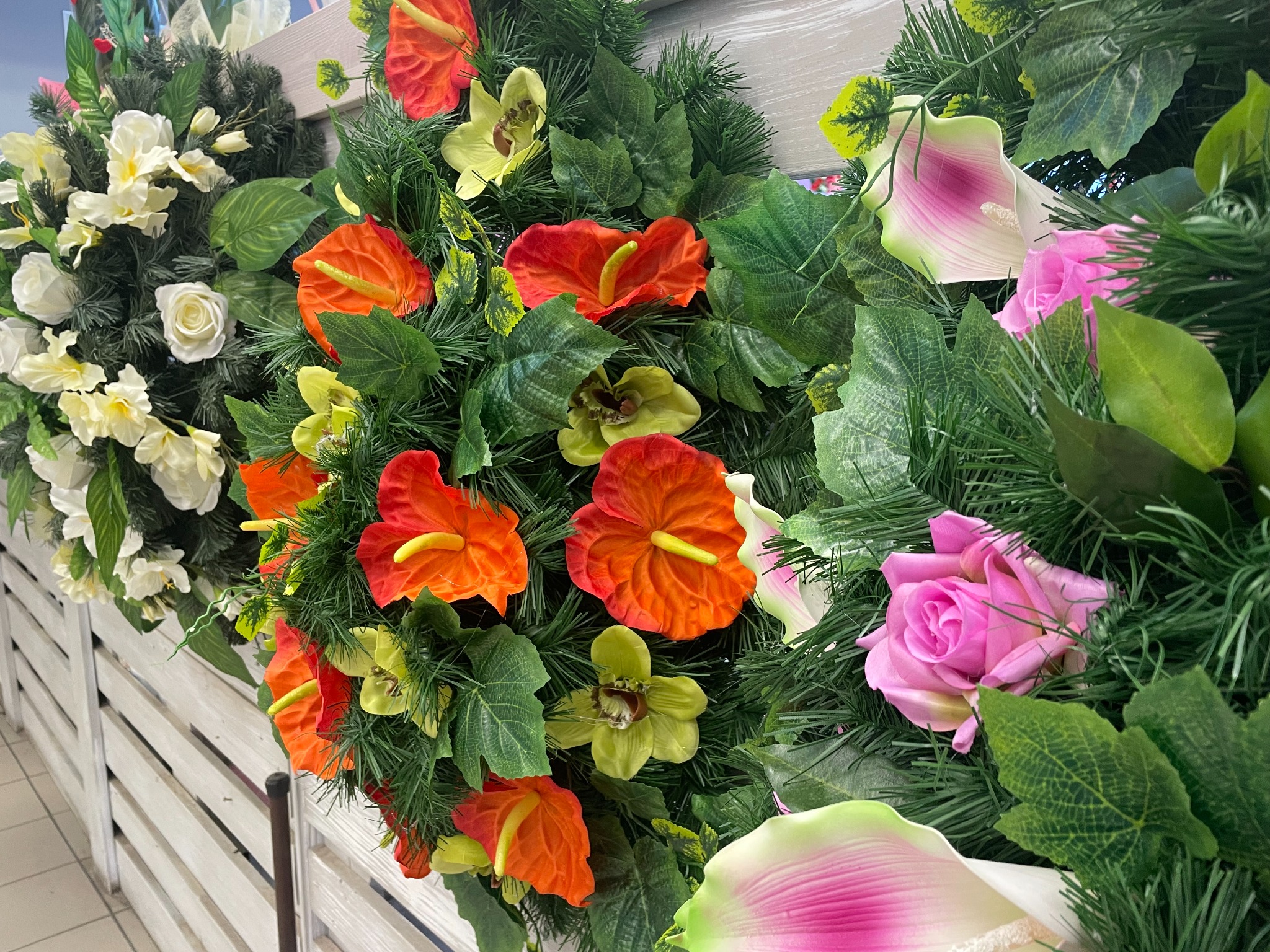 Dekoracja kwiatowa z anturium, kalii, róż i orchidei na tle białego płotu z desek.