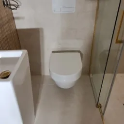 Nowoczesna łazienka z podwieszaną miską WC, umywalką nablatową i kabiną prysznicową z złotymi profilami.