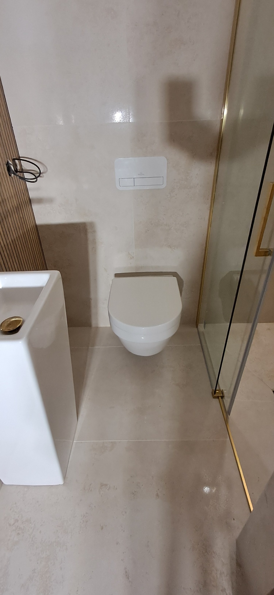 Nowoczesna łazienka z podwieszaną miską WC, umywalką nablatową i kabiną prysznicową z złotymi profilami.