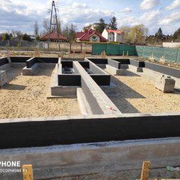 Quick Build - Zalane fundamenty domu z hydroizolacją, widoczne zbrojenia i bloczki betonowe na placu budowy w słoneczny dzień.