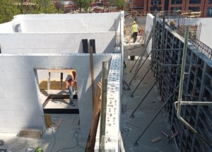 Budowa domu z białych bloczków: widok z góry na wznoszone ściany i szalunki fundamentowe, pracownicy w kaskach na placu budowy.