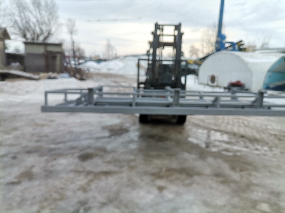 Wózek widłowy przewożący metalową konstrukcję na zewnątrz, w tle budynek i pozostałości śniegu.