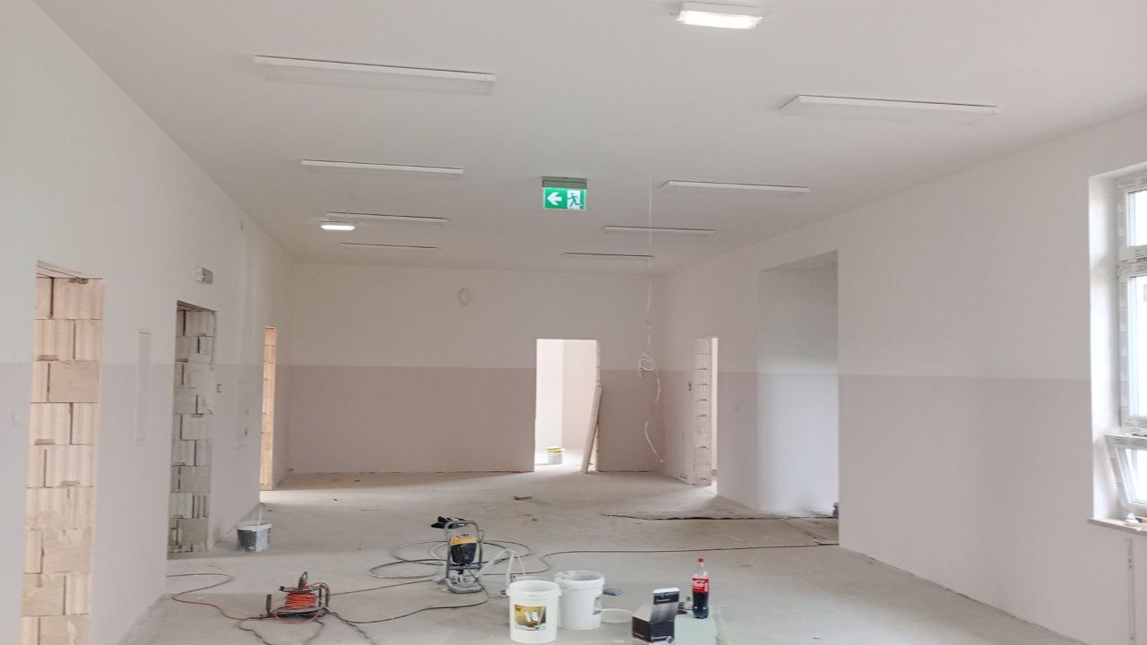 Wnętrze biura w Kącku po częściowym malowaniu ścian na biało i szaro, widoczne narzędzia malarskie i przygotowane pomieszczenie.