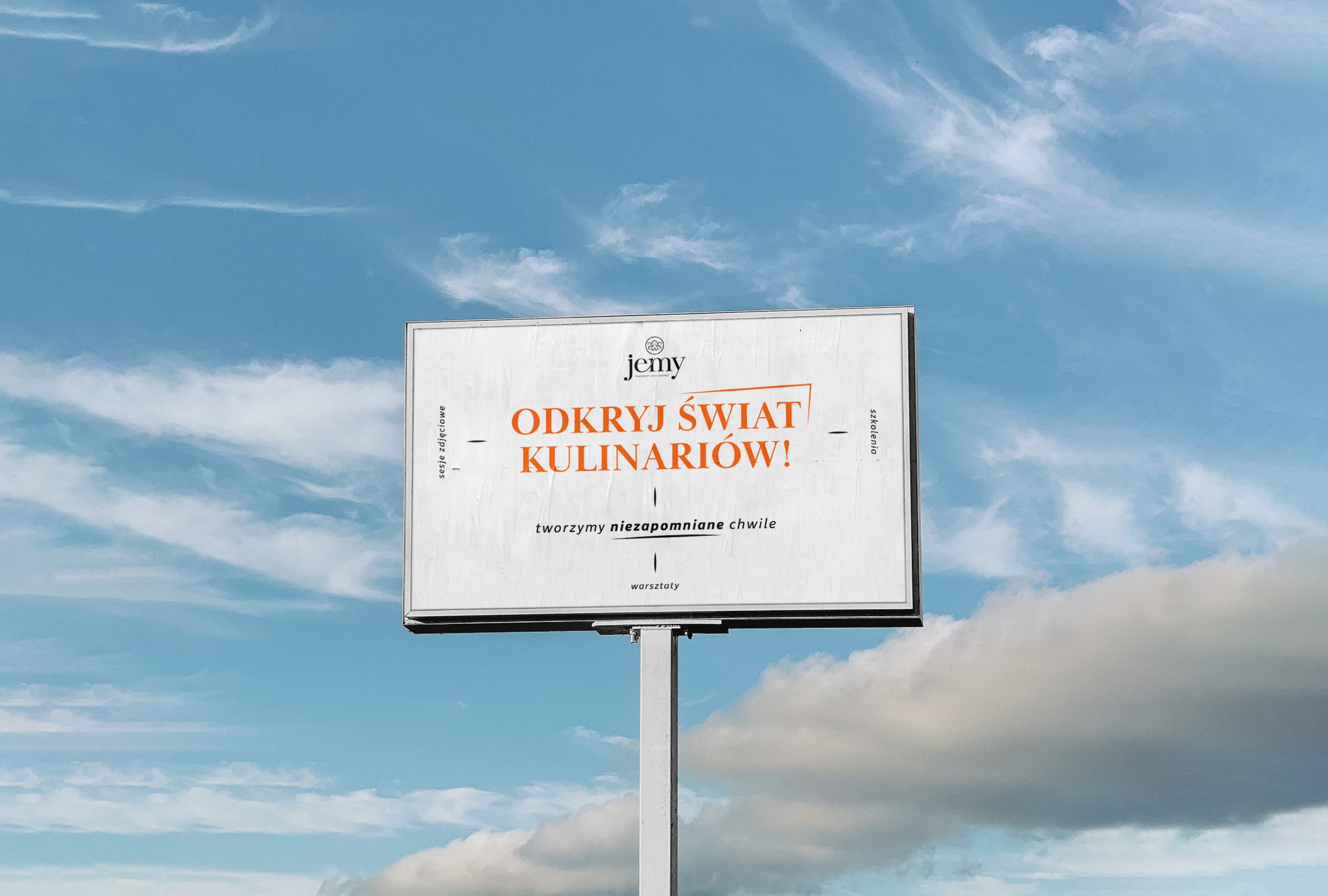 Billboard reklamujący warsztaty kulinarne na tle błękitnego nieba z chmurami. Napis 'Odkryj świat kulinariów!' w kolorze pomarańczowym.