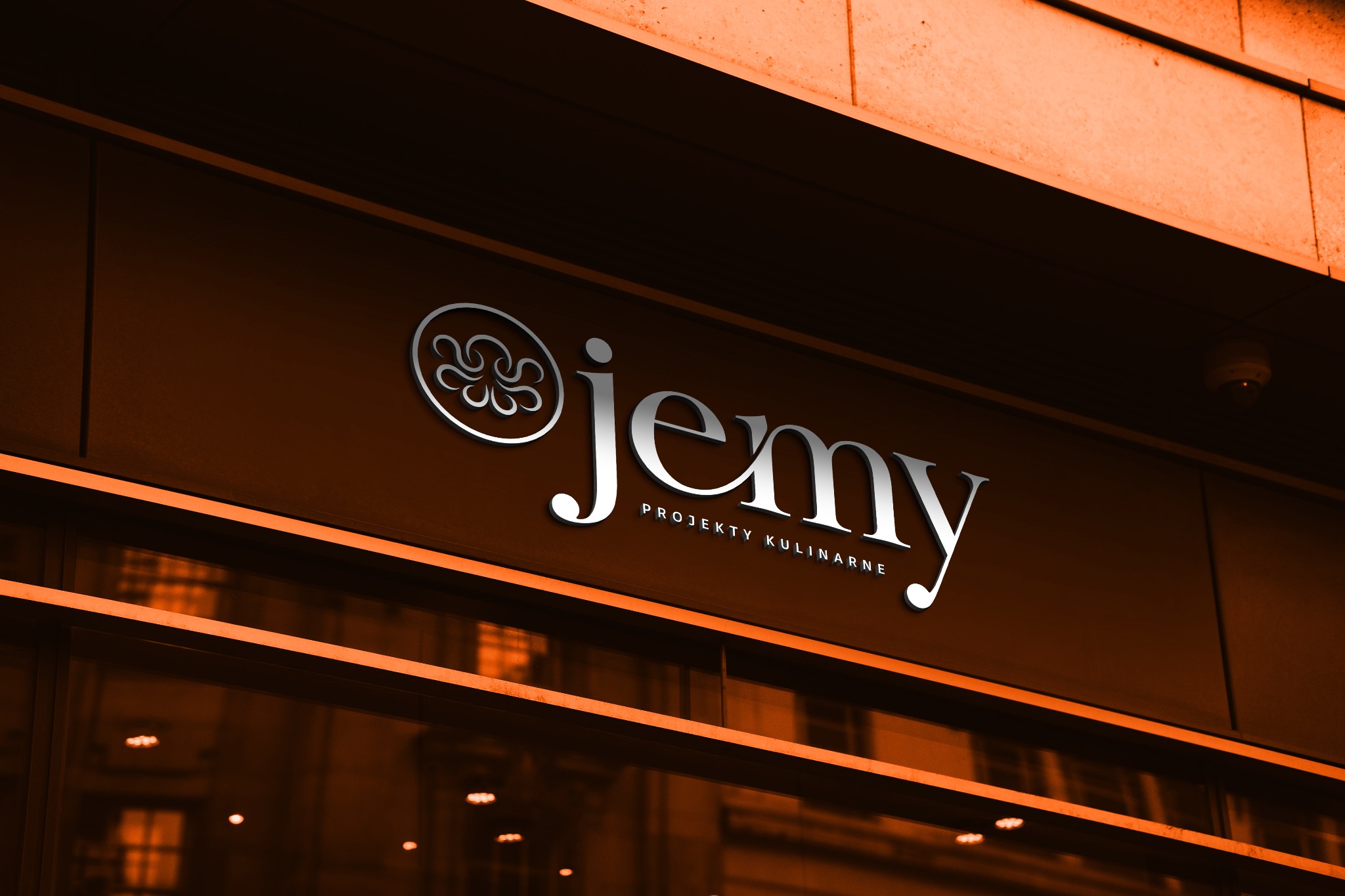 Elegancki szyld z logo 'jemy. PROJEKTY KULINARNE' na brązowej fasadzie budynku, widoczne odbicia w oknach.