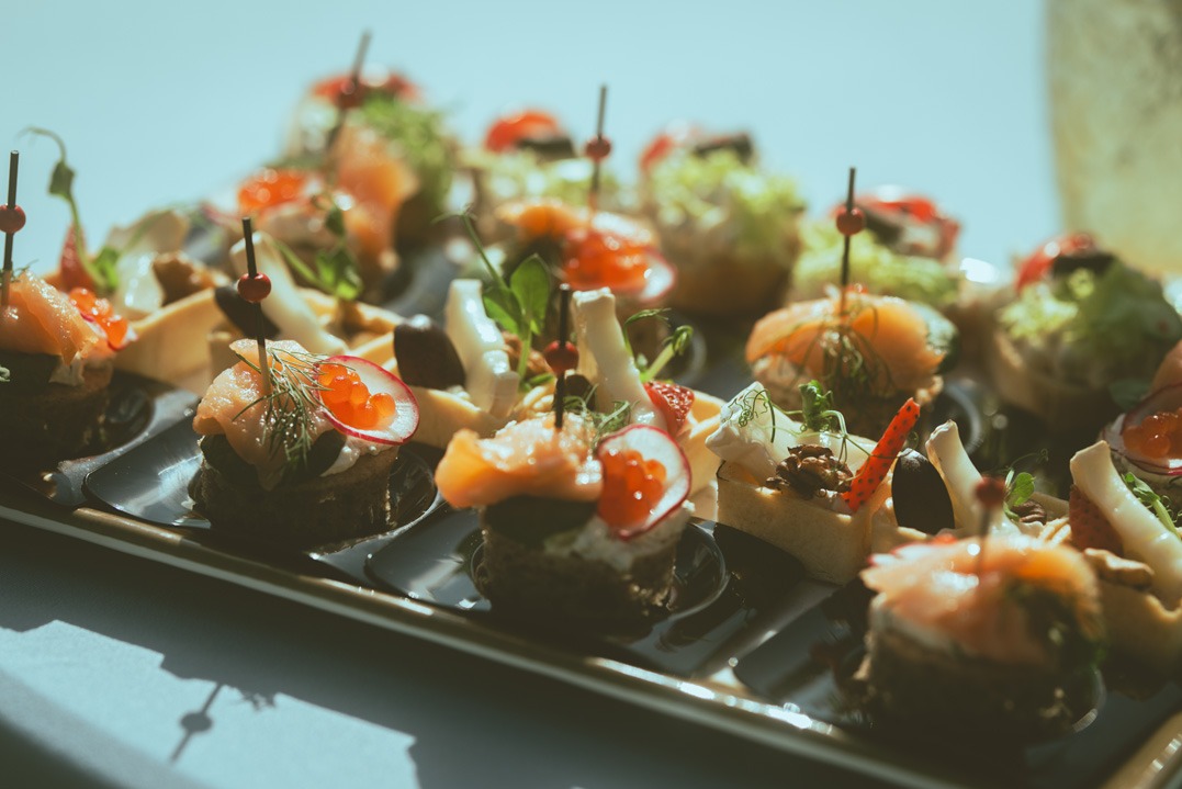 Eleganckie kanapeczki z łososiem, kawiorem i warzywami na ciemnej tacy, oświetlone naturalnym światłem, tworzące apetyczną kompozycję.