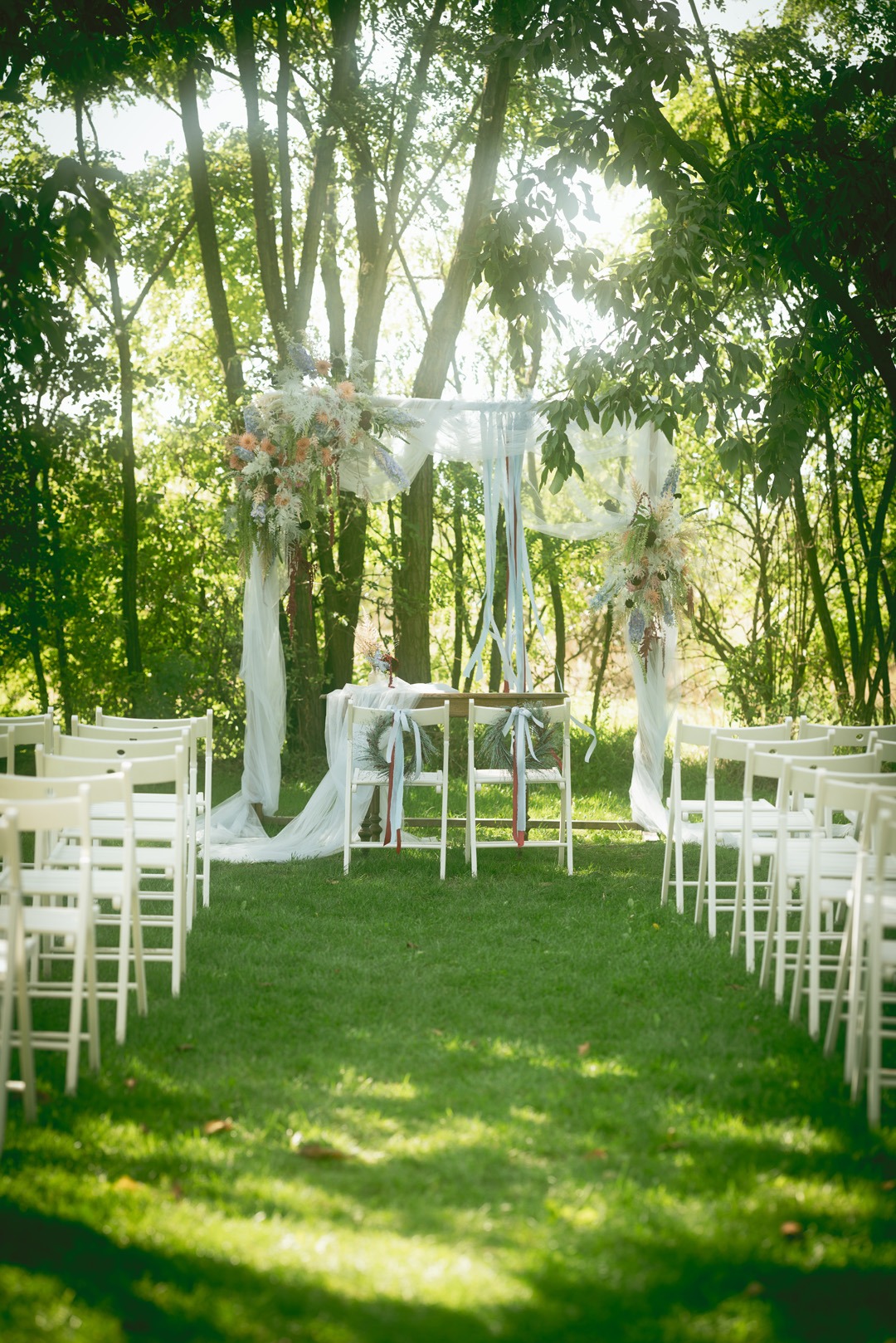 Romantyczna aranżacja ślubna w plenerze w Warszawie. Białe krzesła i dekorowany kwiatami baldachim tworzą wyjątkową atmosferę ceremonii.