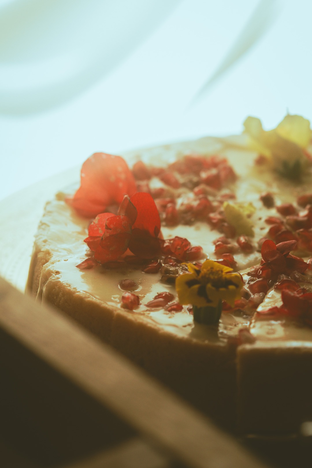 Kremowy tort z dekoracją z jadalnych kwiatów i owoców granatu, prezentowany z bliska, z delikatnym oświetleniem podkreślającym detale.