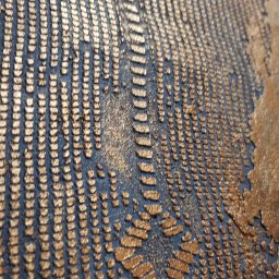 Styloteka - Abstrakcyjna tekstura ściany z metalicznymi, złotymi wypukłościami na ciemnym tle, tworzącymi geometryczny wzór przypominający ślady pędzla.