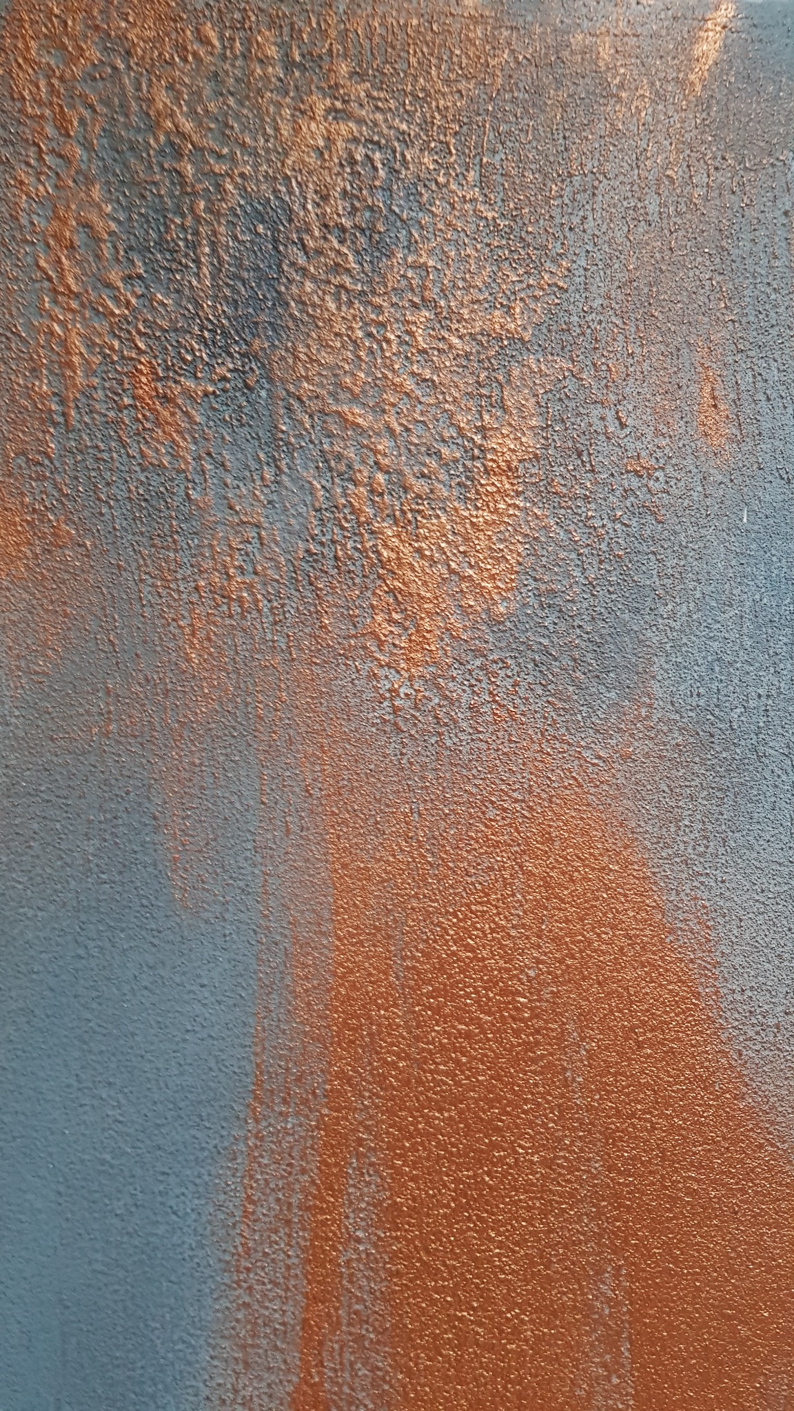 Tekstura ściany z efektem ombre, przechodząca od szarego do miedzianego, z widoczną strukturą farby.