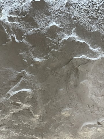 Szpachlowana, nierówna powierzchnia ściany w odcieniach bieli i szarości, widoczne liczne zagłębienia i wypukłości, surowe wykończenie wnętrza.