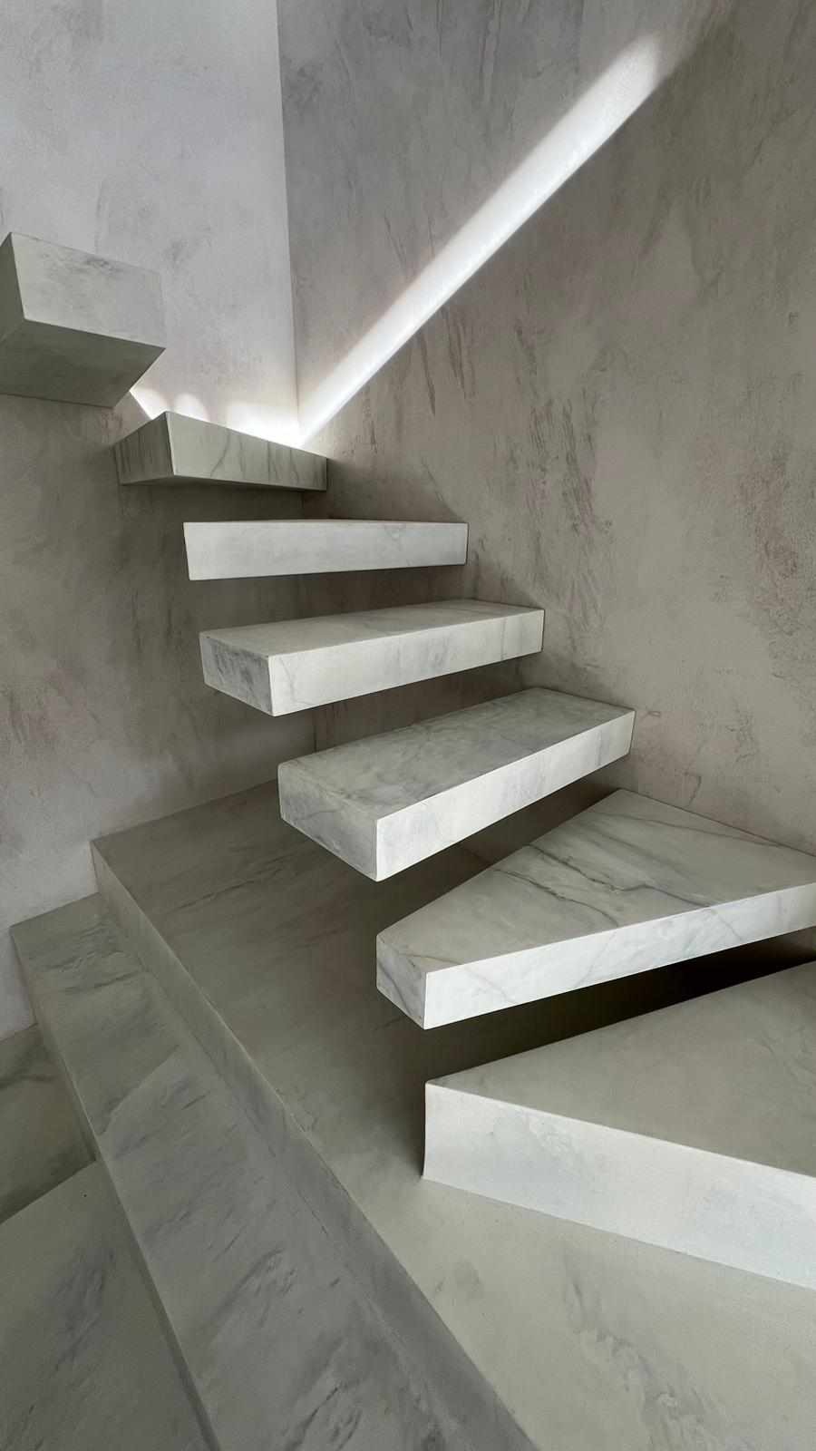 Nowoczesne, marmurowe schody wspornikowe z podświetleniem LED w minimalistycznym wnętrzu z szarą, teksturowaną ścianą.