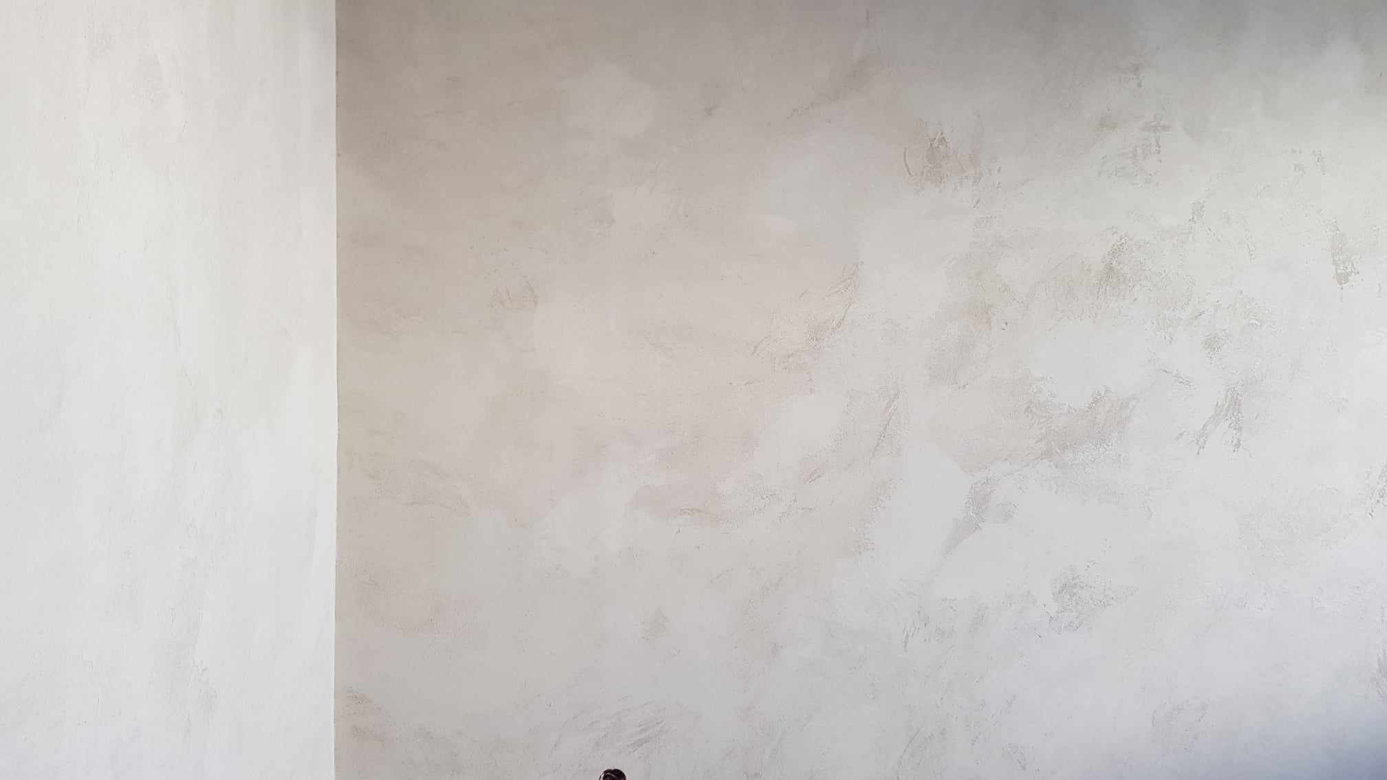 Ściana w pokoju po nałożeniu dekoracyjnej, jasnej farby z efektem przecierki, widoczny narożnik pomieszczenia.