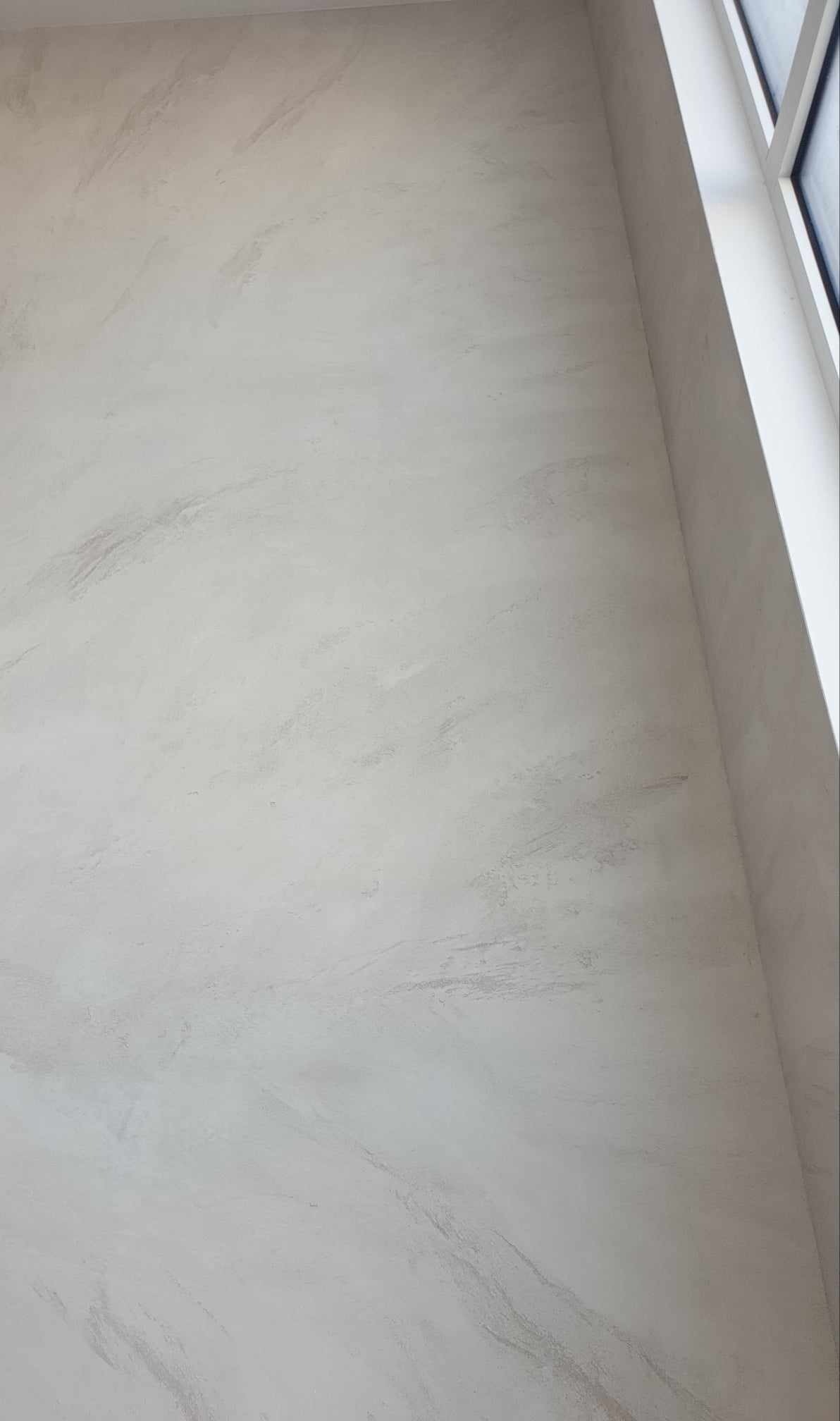 Ściana w jasnych odcieniach beżu i szarości z efektem marmuru, widoczna część okna z białymi ramami.