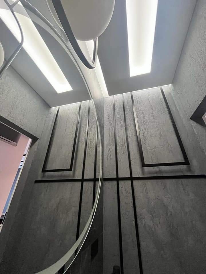 Nowoczesne oświetlenie sufitowe z dekoracyjnymi czarnymi listwami na szarej, teksturowanej ścianie, widok z dołu.