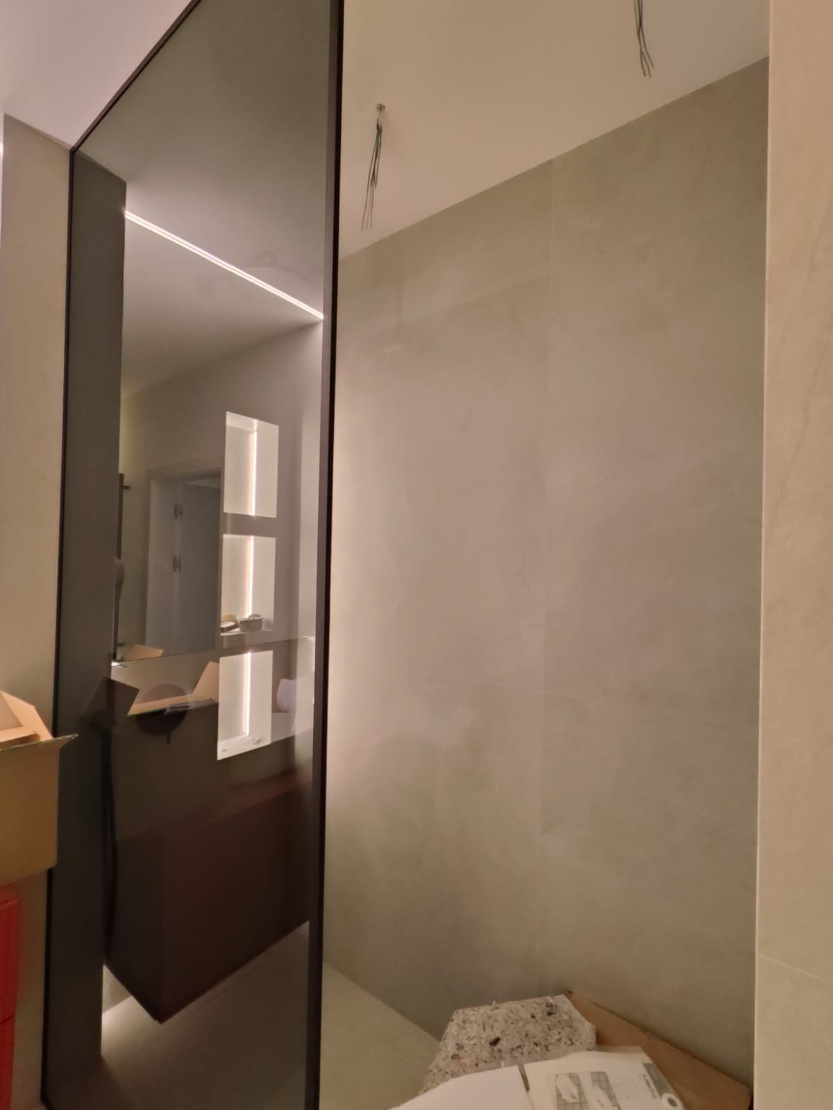 Wystające kable sufitowe w łazience z zamontowaną szklaną ścianką prysznicową i oświetleniem LED w lustrze.