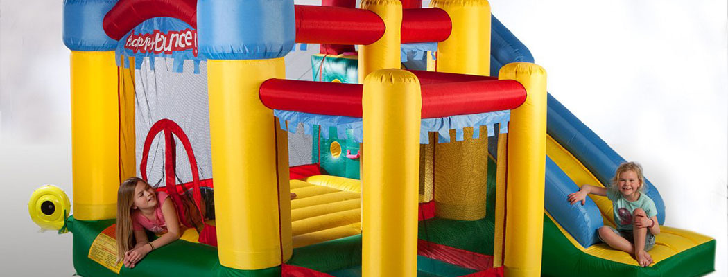 Dwie dziewczynki bawią się w kolorowym zamku dmuchanym z motywem Happy Bounce, jedna leży w dolnej części, druga siedzi na zjeżdżalni.