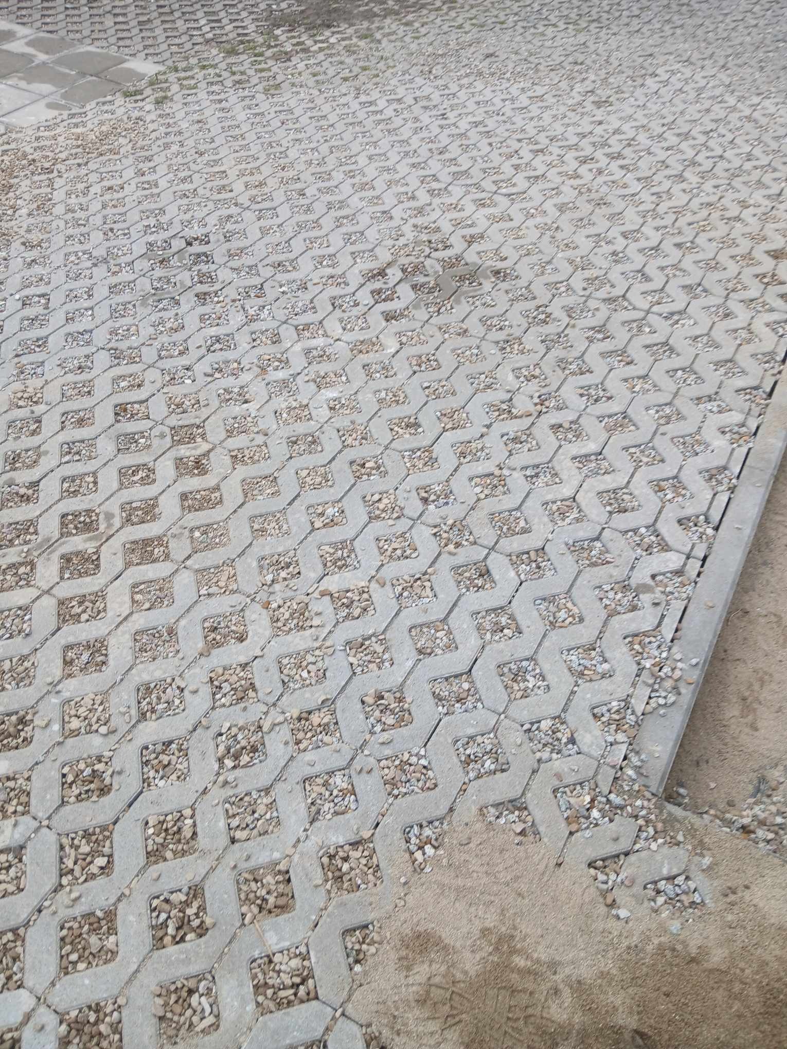 Szara, ażurowa kostka brukowa wypełniona drobnym żwirem na podjeździe, widok z góry.