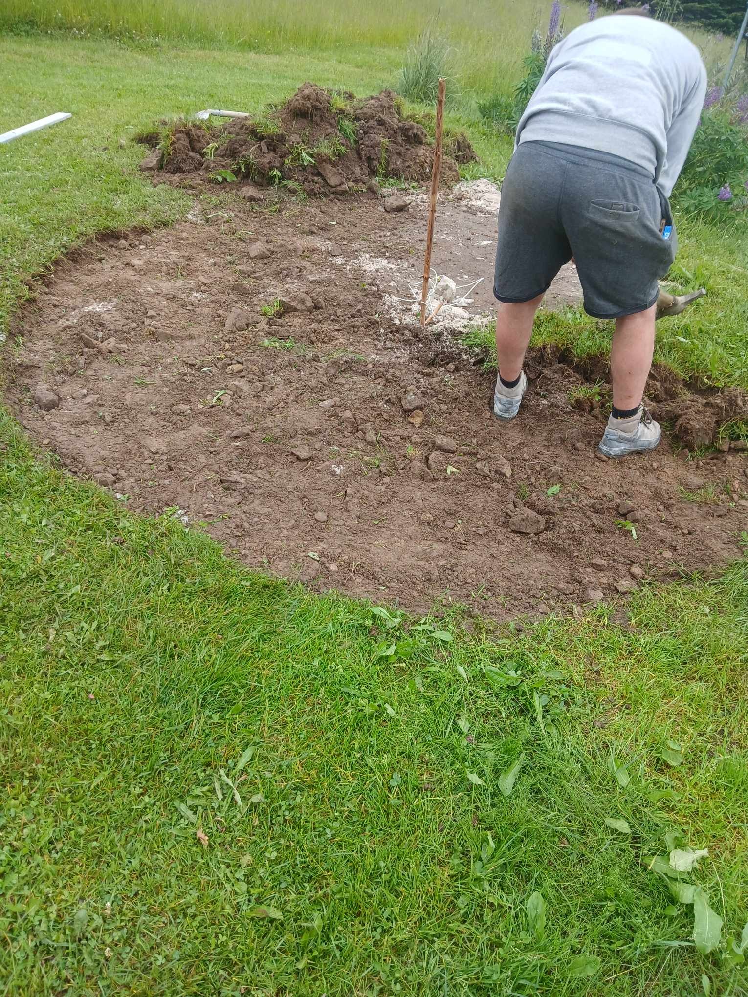 Przygotowanie terenu pod budowę, widoczne wyznaczone granice obszaru i osoba pracująca łopatą w ogrodzie.