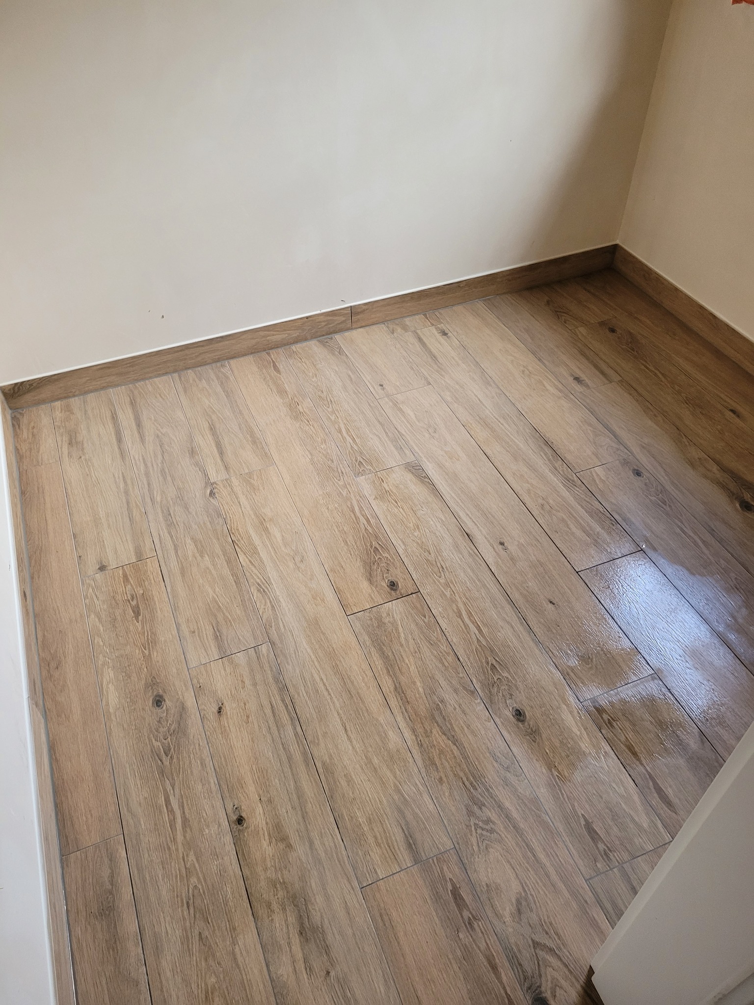 Ułożona podłoga z płytek imitujących drewno, widok z góry, jasne ściany i listwy przypodłogowe.