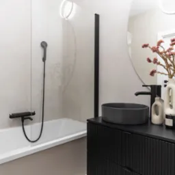 Nowoczesna łazienka z czarną armaturą i umywalką nablatową. Minimalistyczny design, beżowe płytki, okrągłe lustro i dekoracyjne akcenty.