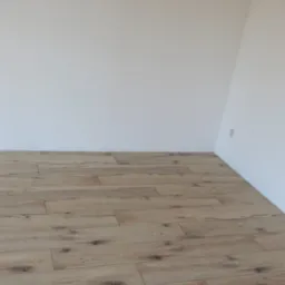 Jasne panele podłogowe ułożone w nowym pomieszczeniu z białymi ścianami i gniazdkiem elektrycznym