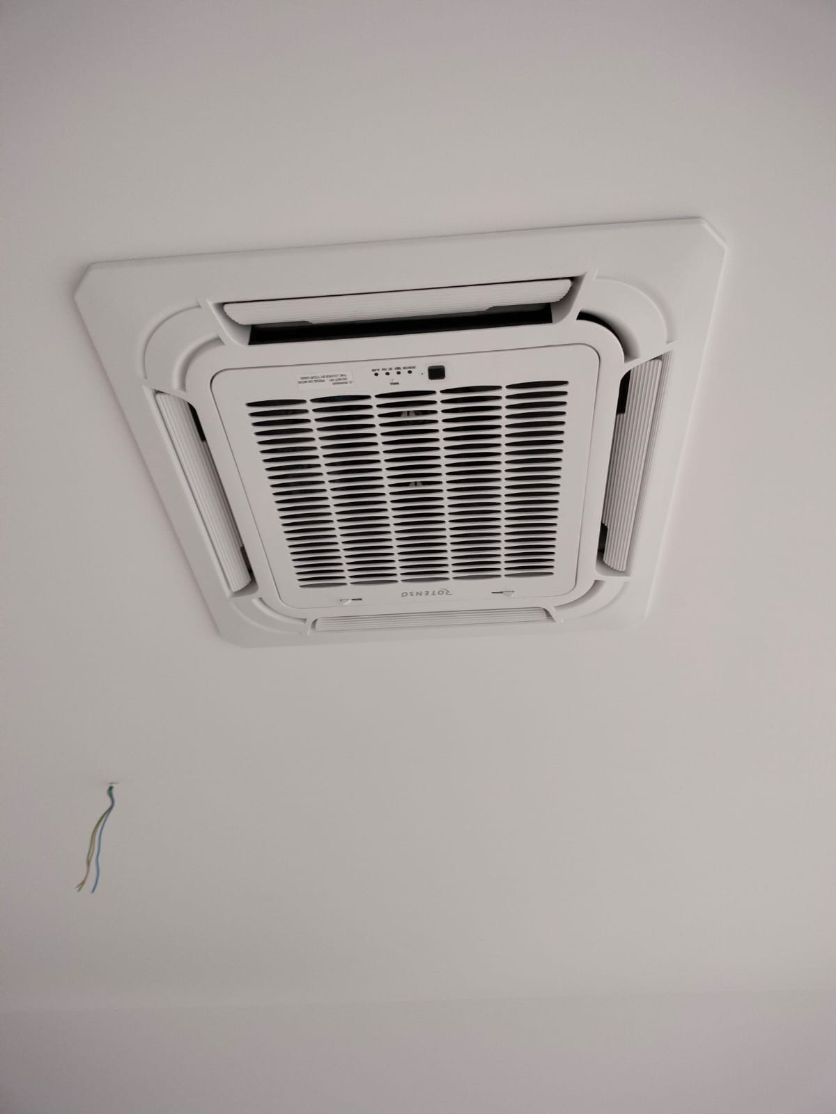 Biała, sufitowa klimatyzacja kasetonowa marki Rotenso, widoczne niedokończone podłączenie elektryczne w postaci wystających przewodów ze ściany.