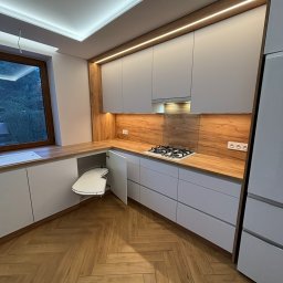 MCH Projekt Meble - Nowoczesna kuchnia w Krakowie z szarymi frontami i drewnianym blatem. Widoczny system narożny z półkami obrotowymi. Oświetlenie LED podkreśla detale.