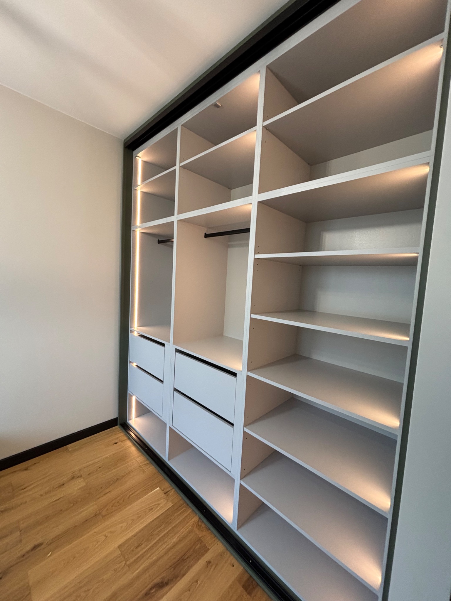 Szafa wnękowa z przesuwnymi drzwiami i oświetleniem LED, widok od dołu z parkietem na podłodze.