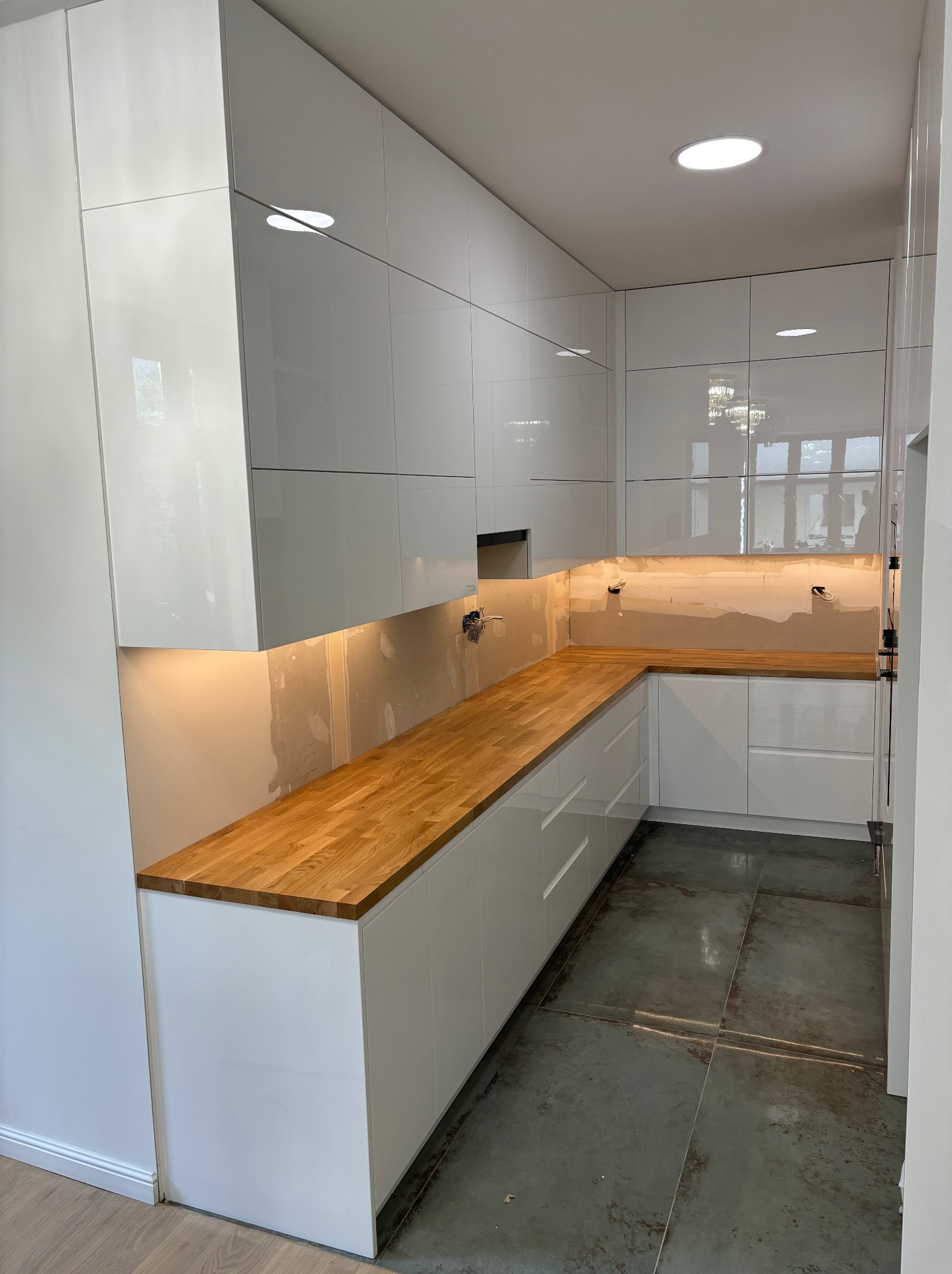 Montaż białej, lakierowanej kuchni w Krakowie z drewnianym blatem, widoczne niedokończone prace wykończeniowe na ścianie nad blatem.