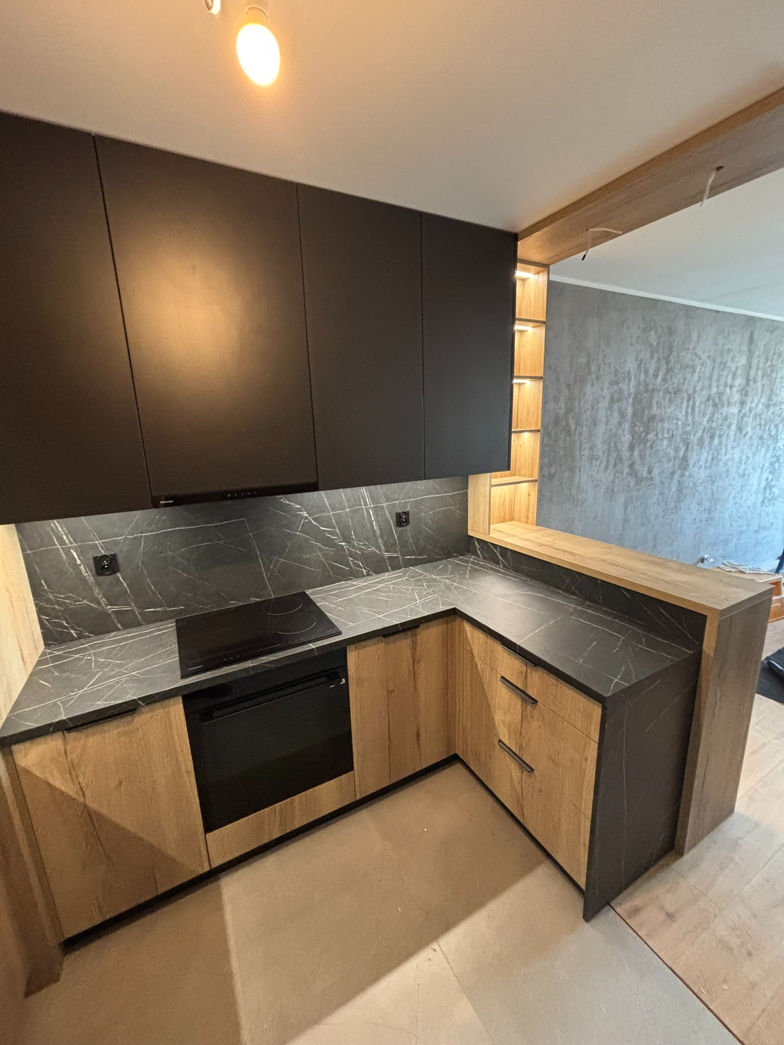 Nowoczesna kuchnia w odcieniach drewna i grafitu, z blatem imitującym marmur i oświetleniem LED w półce, tworząca spójną, elegancką przestrzeń.