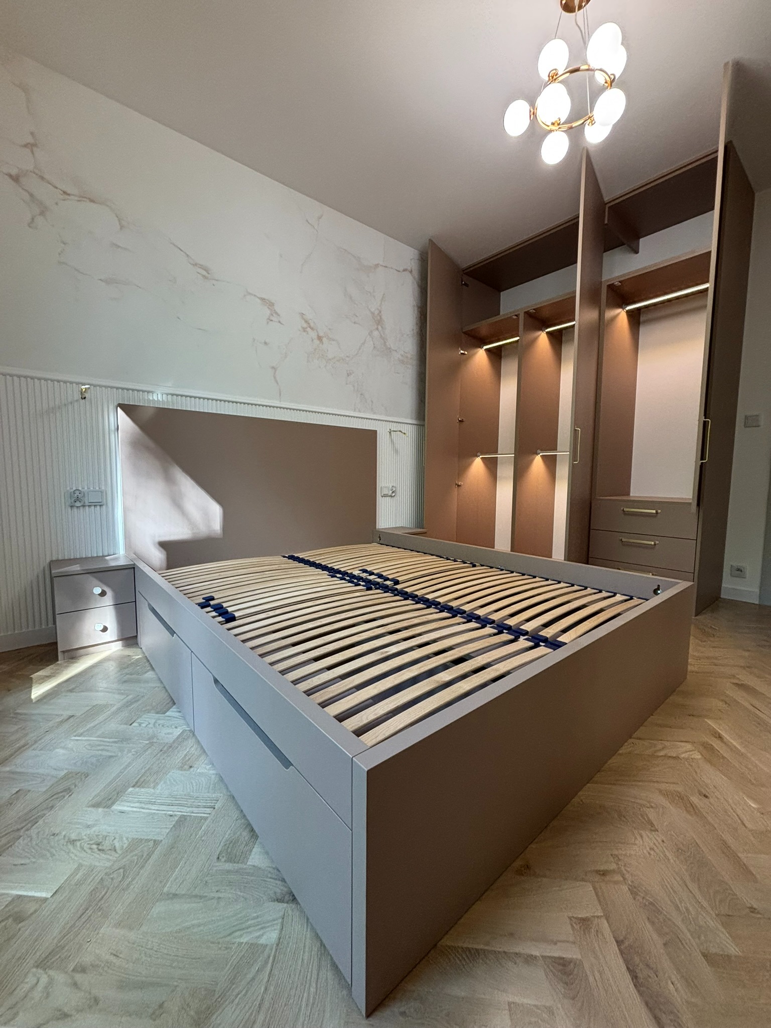 Sypialnia z łóżkiem z szufladami i szafą wnękową z oświetleniem LED. Parkiet w jodełkę, marmurowa ściana i designerska lampa.