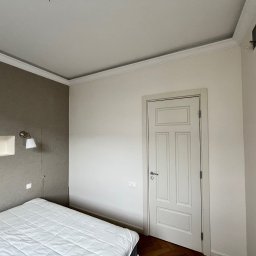 Firma Remontowo-Budowlana DAW-BUD Dawid Bala - Ściana w sypialni pomalowana na dwa kolory: szary z lewej strony i biały z prawej, z białą, klasyczną stolarką drzwiową i parkietem w jodełkę.