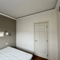 Ściana w sypialni pomalowana na dwa kolory: szary z lewej strony i biały z prawej, z białą, klasyczną stolarką drzwiową i parkietem w jodełkę.