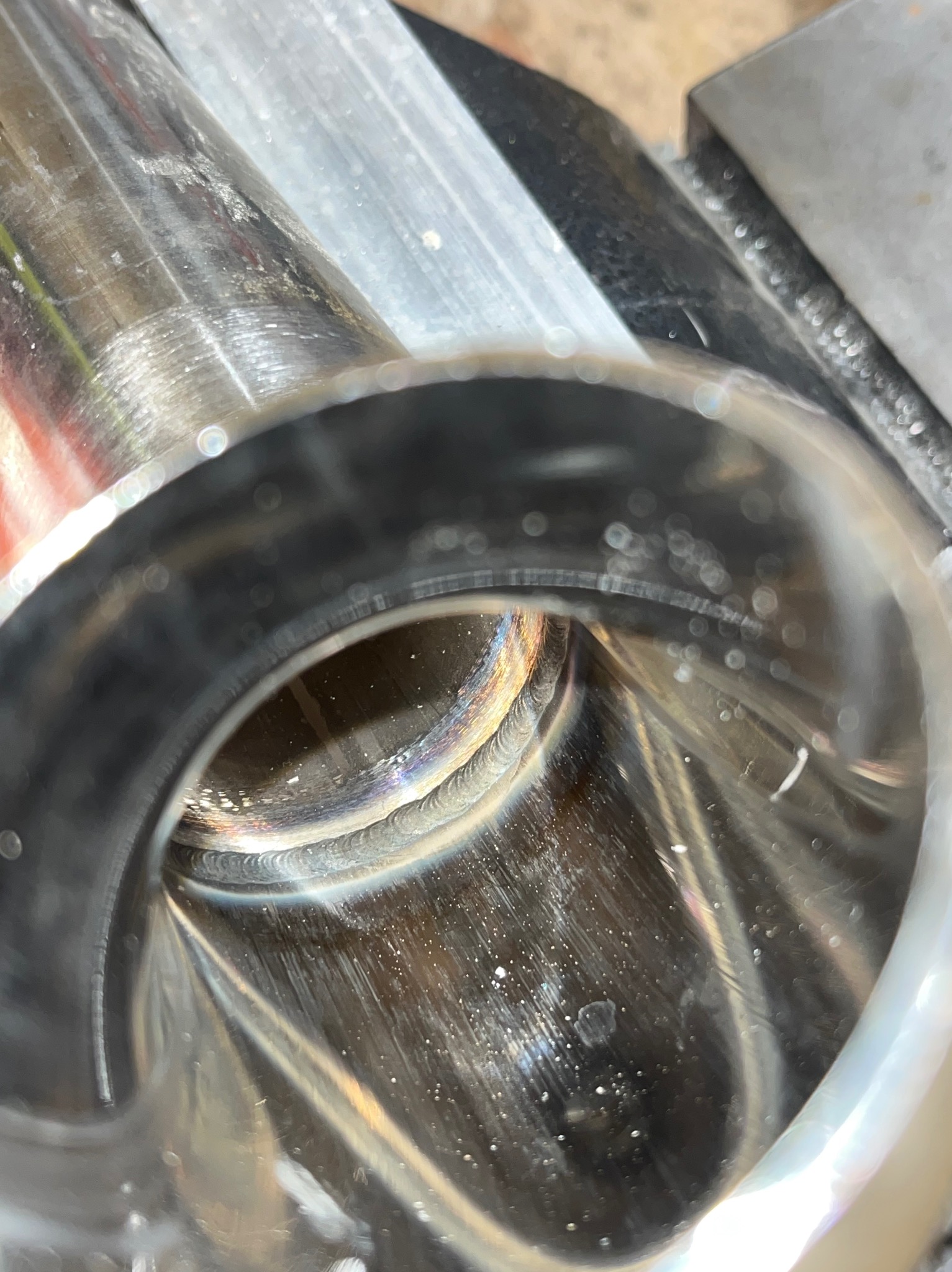 Wnętrze rury ze stali nierdzewnej z widocznym spoiwem po procesie łączenia, zamocowanej w uchwycie. Widoczne ślady obróbki i refleksy świetlne.