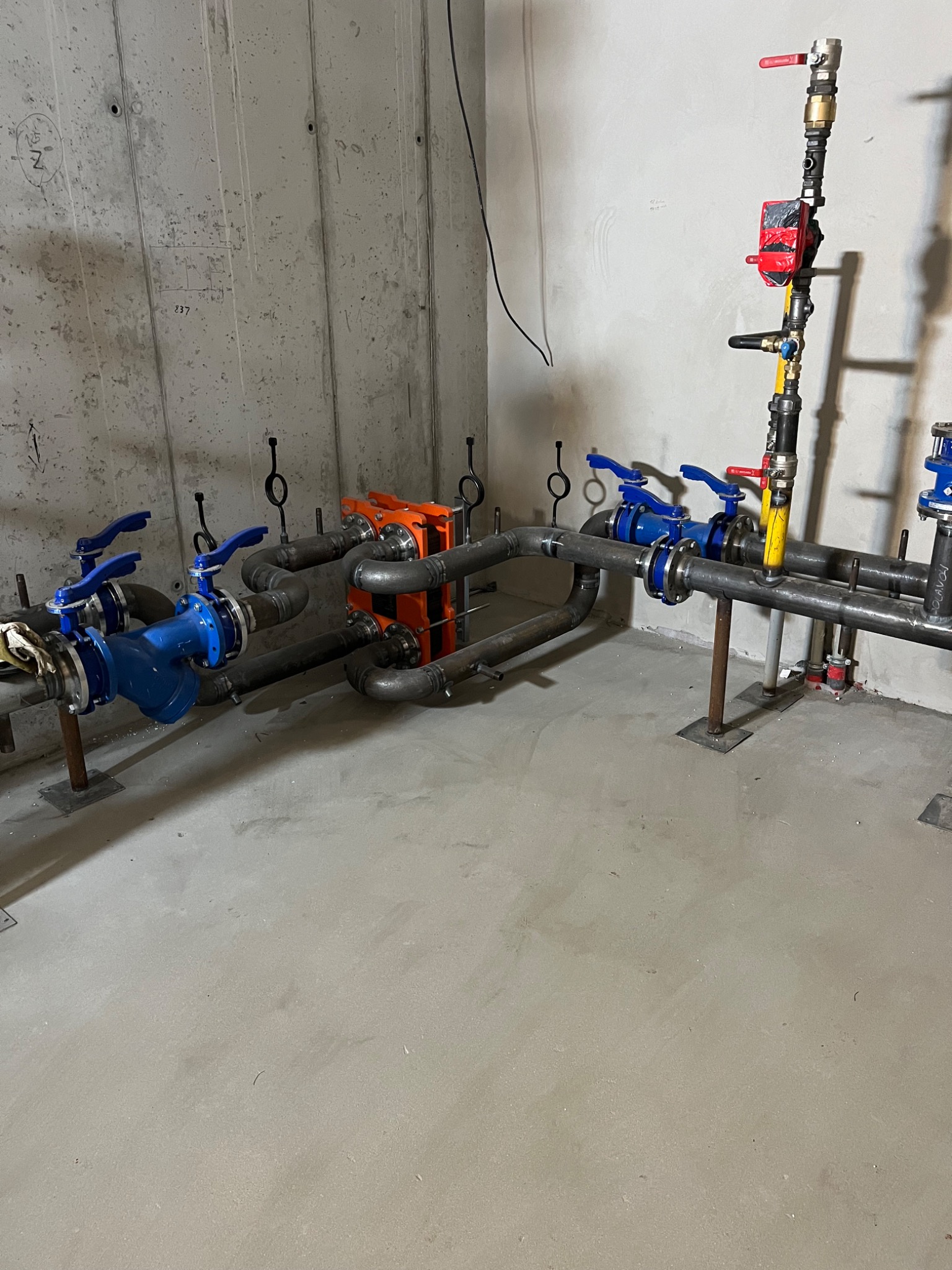 Instalacja przemysłowa z rur, zaworów i wymiennika ciepła w surowym pomieszczeniu z betonowymi ścianami.