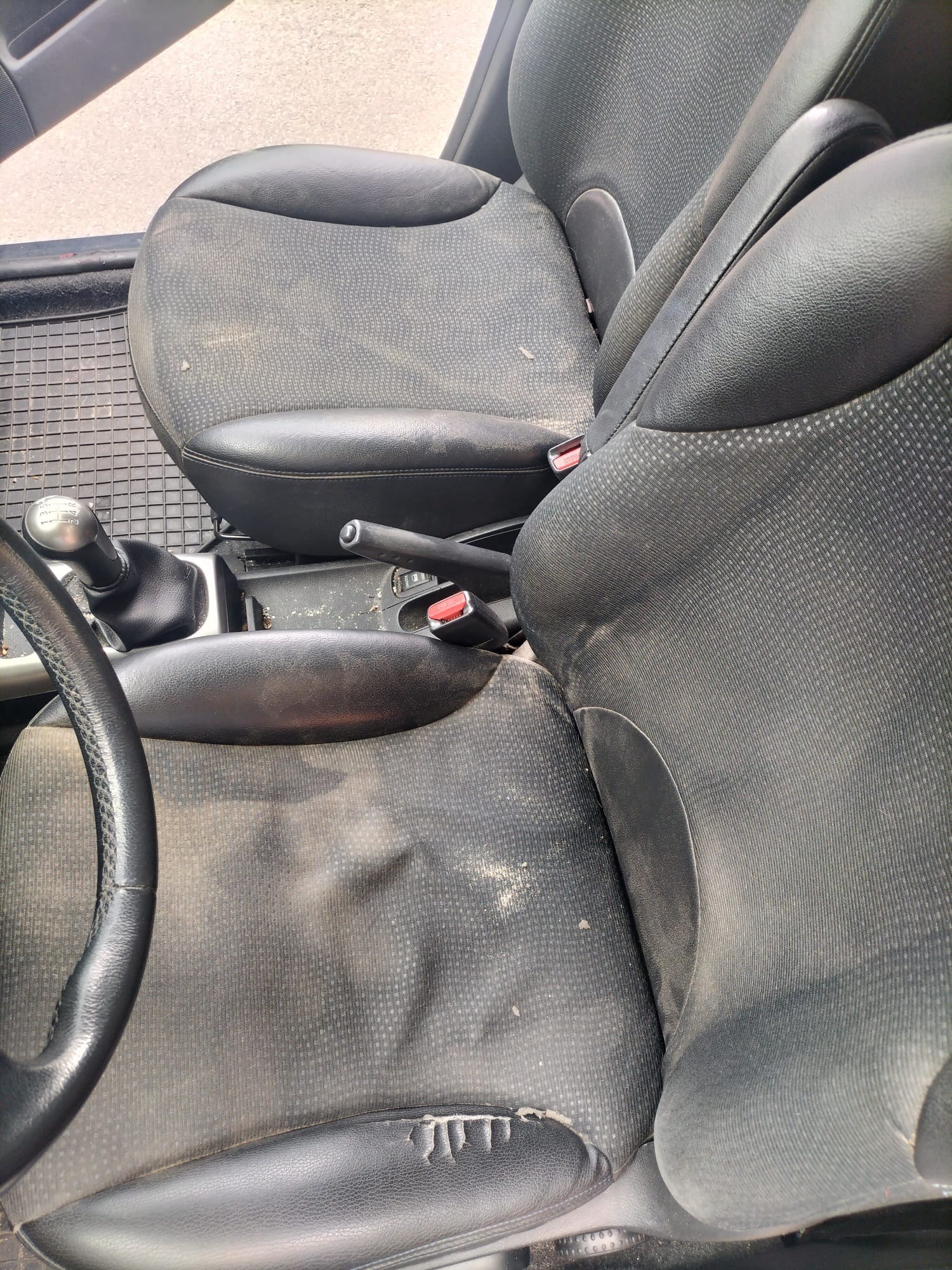 Bardzo zabrudzone, czarne fotele samochodowe z widocznymi plamami i uszkodzeniami tapicerki, wnętrze pojazdu.