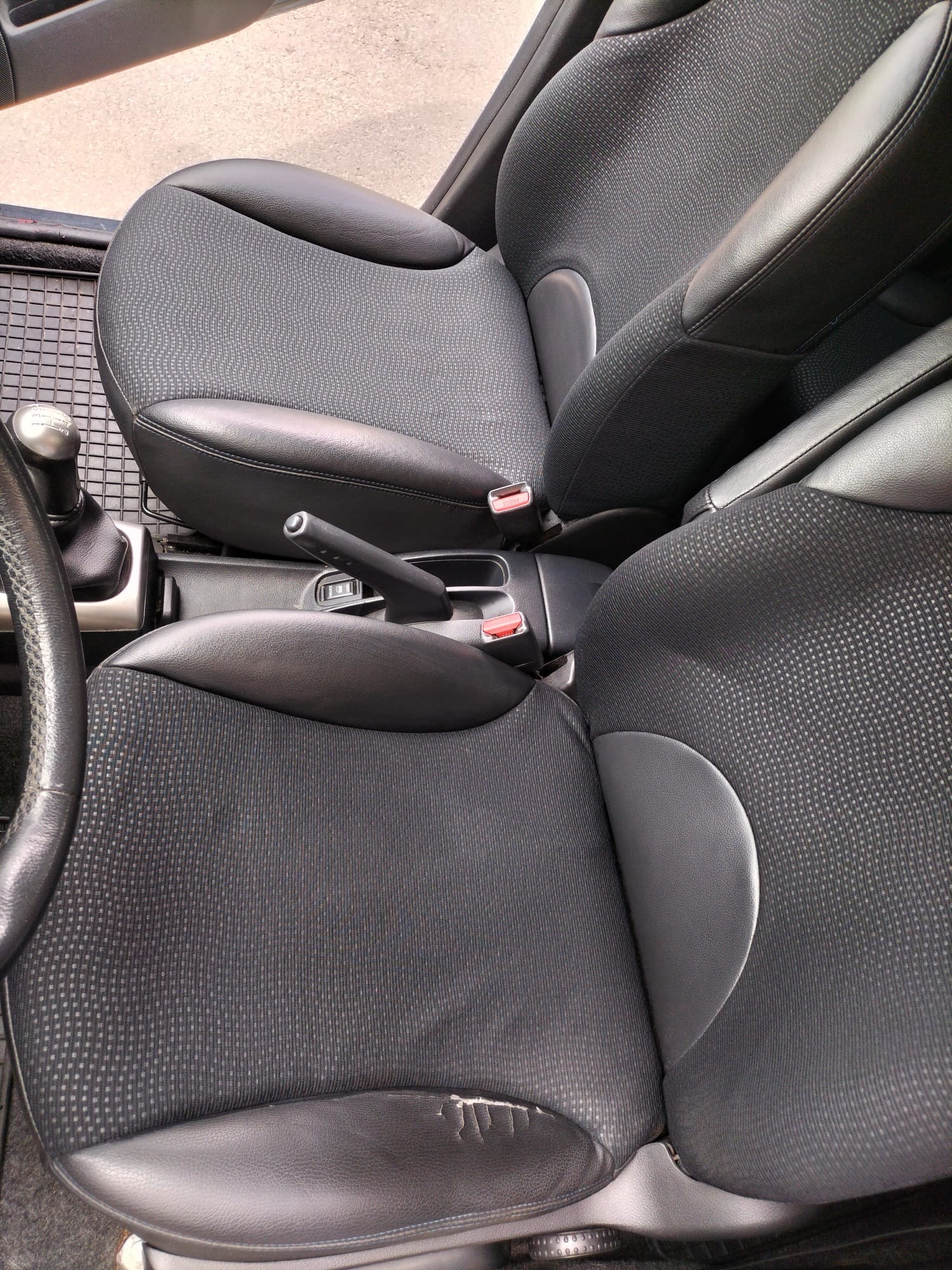 Czarne, materiałowo-skórzane fotele samochodowe z widocznym uszkodzeniem tapicerki na jednym z siedzeń.