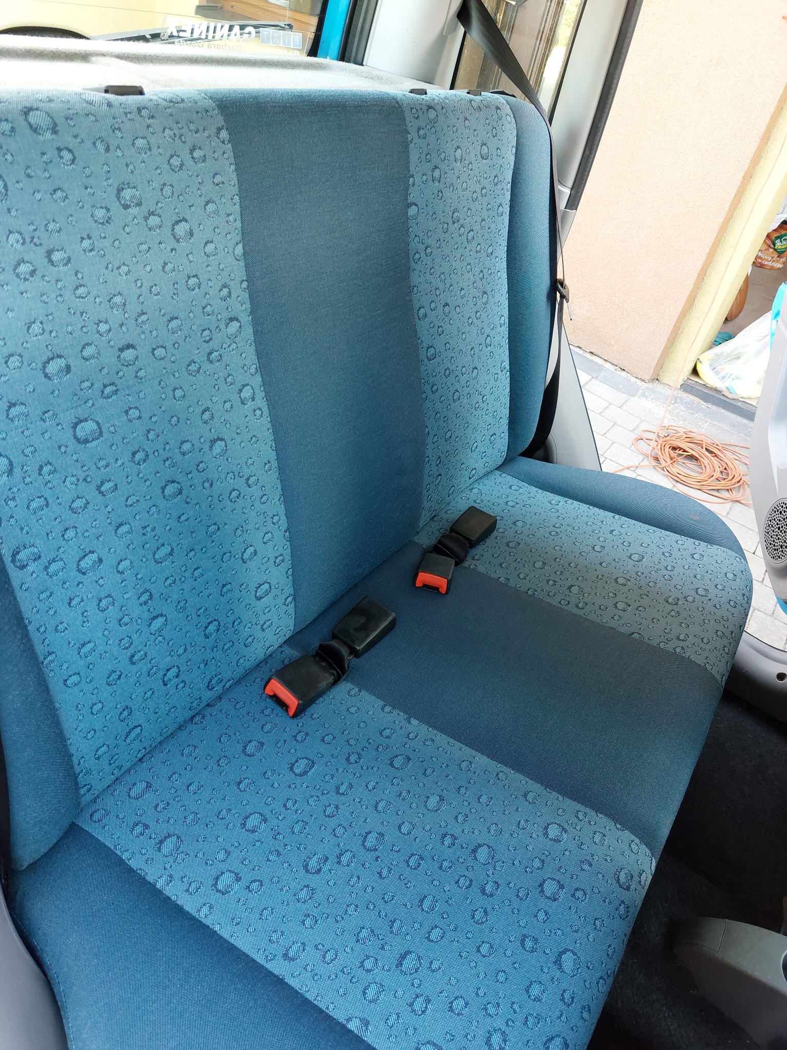 Błękitne siedzenie samochodu z wzorem kropelek wody i zapiętym pasem bezpieczeństwa, widok z wnętrza pojazdu.