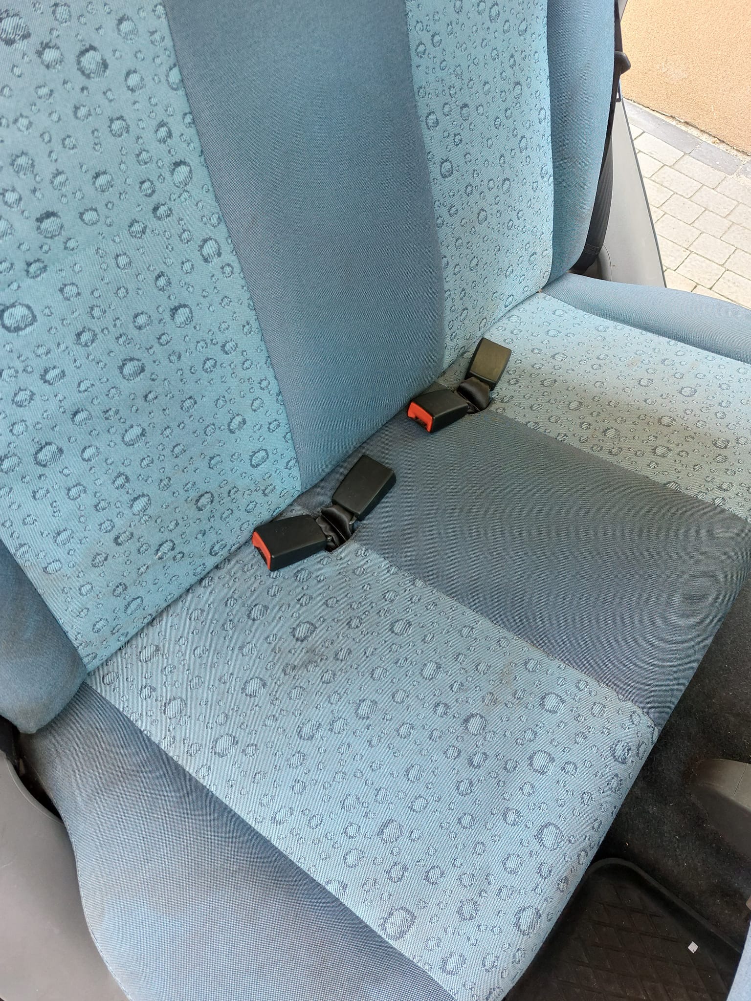 Błękitne, dwukolorowe siedzenie samochodowe z wzorem kropelek wody i rozpiętymi pasami bezpieczeństwa.