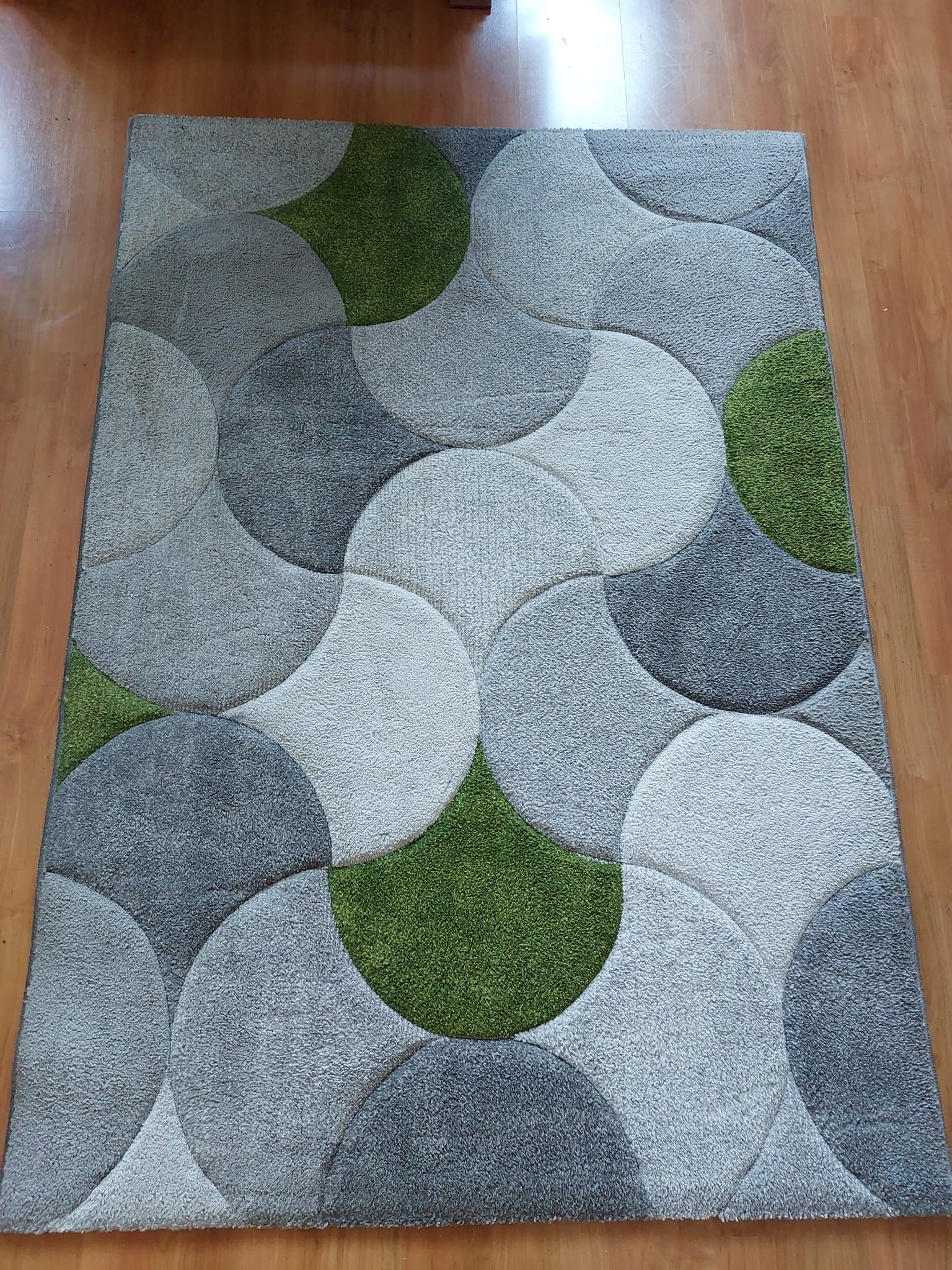 Wzorzysty dywan z motywem nakładających się szarych i zielonych półokręgów na drewnianej podłodze.