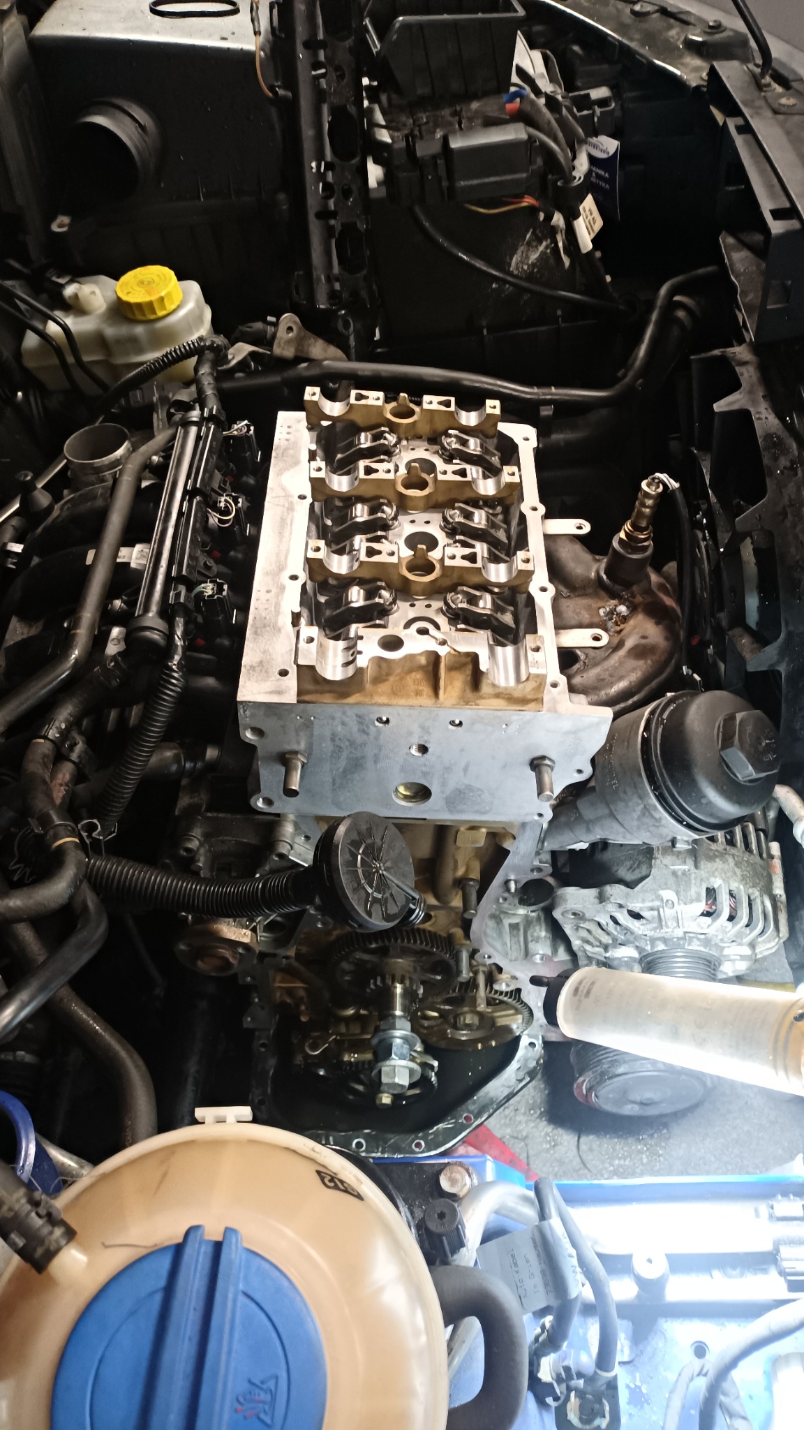 Widok z góry na silnik samochodowy w trakcie naprawy, z widoczną głowicą cylindrów, wałkami rozrządu i elementami osprzętu, oświetlony lampą warsztatową.