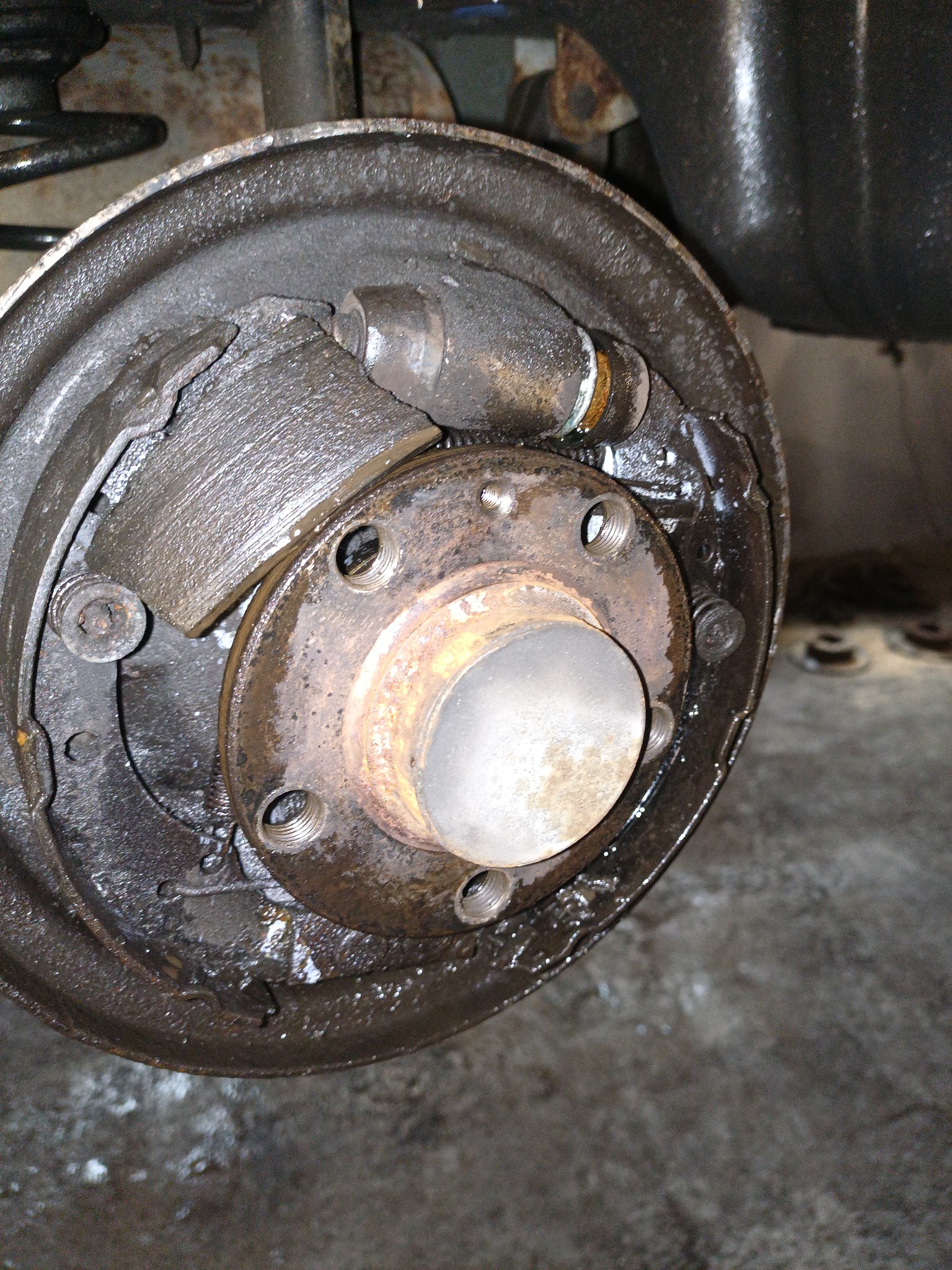 Detail of a disassembled, heavily worn and greasy drum brake system with visible brake shoes, wheel cylinder and rusty components.