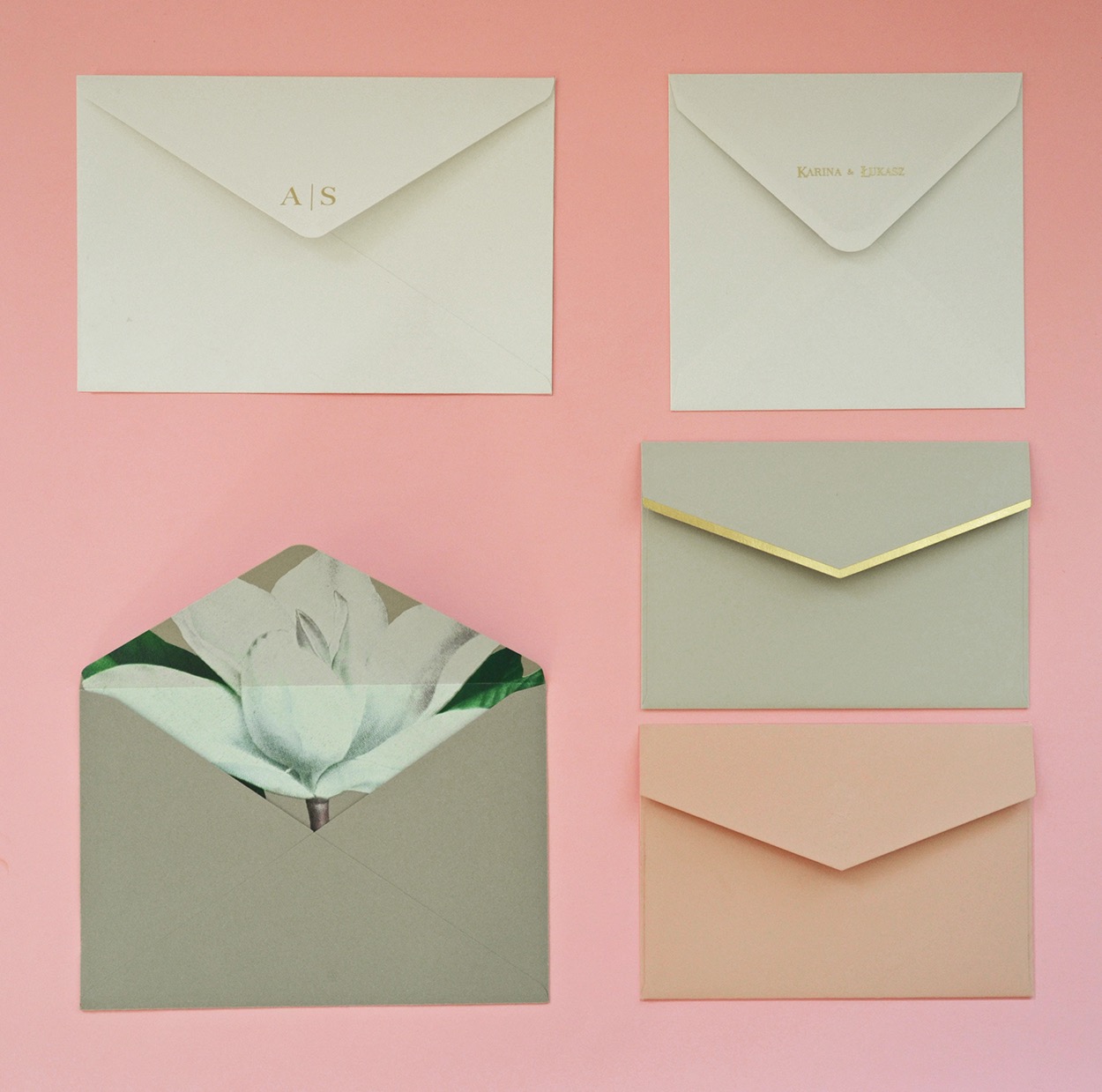 Różnokolorowe, eleganckie koperty z różnymi motywami i napisami na jasnoróżowym tle, jedna z kopert otwarta z widocznym motywem kwiatowym wewnątrz.