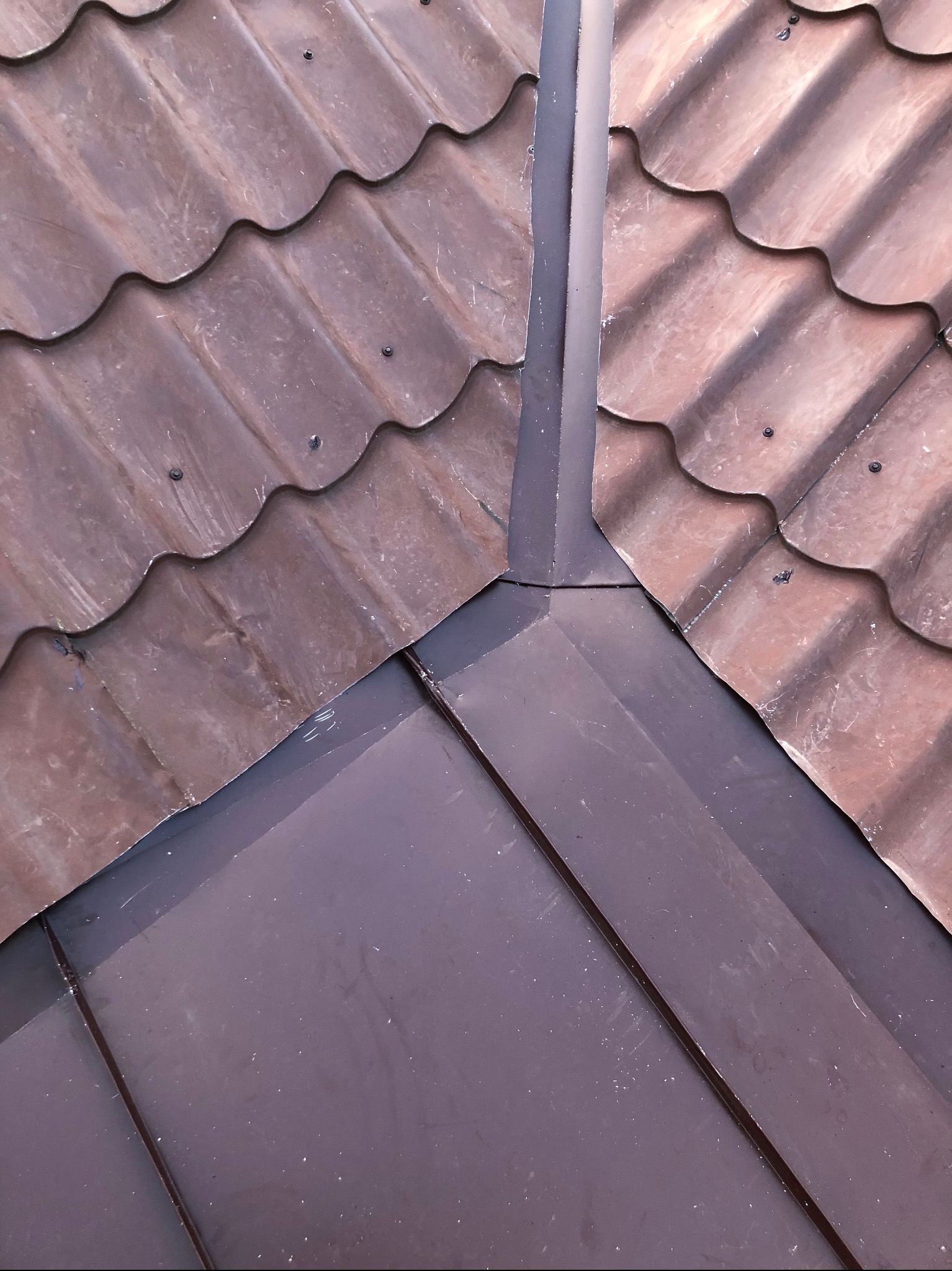 Połączenie falistej dachówki ceramicznej z płaską blachą na dachu, widoczne mocowania, zbliżenie na detale.