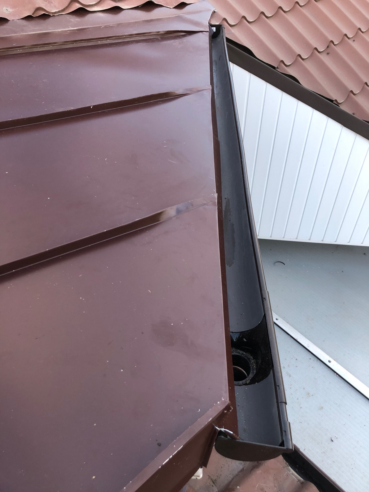 Brązowy dach z blachy trapezowej z zamontowaną czarną rynną, widoczne łączenie rynny z otworem spustowym.